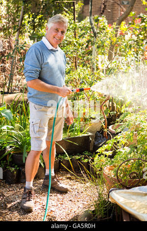 Porträt von Gärtner Pflanzen aus Schlauch im Garten gießen Stockfoto