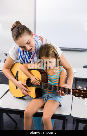 Lehrer helfen Mädchen Gitarrespielen im Klassenzimmer Stockfoto