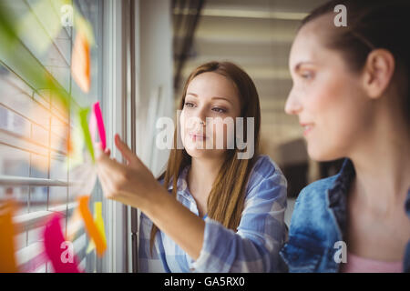 Geschäftsfrau kleben Klebefuge Notizen auf Fenster im Büro Stockfoto