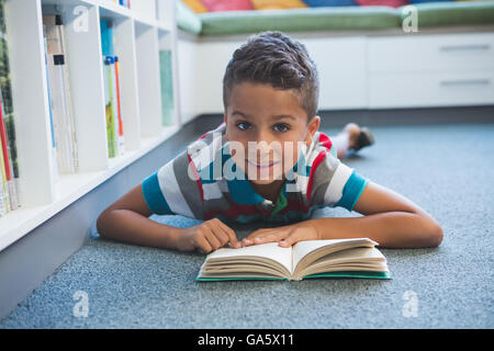 Schüler am Boden liegen und ein Buch in der Bibliothek Stockfoto