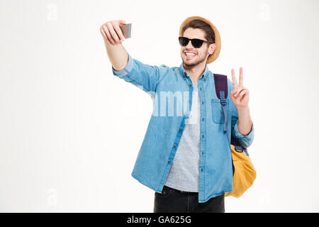 Glücklich Jüngling in Sonnenbrille mit Rucksack macht Selfie und mit Peace-Zeichen Stockfoto