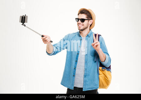 Fröhlichen jungen Mann mit Rucksack fotografieren mit Handys und Selfie stick Stockfoto