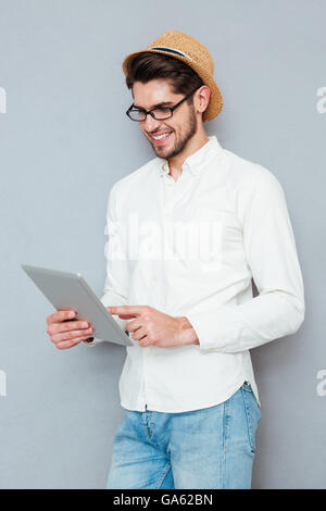 Porträt eines glücklichen jungen Mannes in Brillen mit Tablet-Computer auf einem grauen Hintergrund isoliert Stockfoto