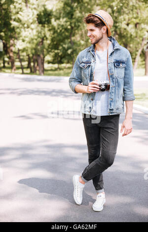 Gut aussehend bärtigen lächelnd Hipster Mann hält Retro-Kamera mit Hut in der Park-Natur Stockfoto