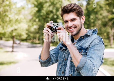 Glücklich, lässig Hipster Mann machen Foto mit Retro-Kamera im Freien im park Stockfoto