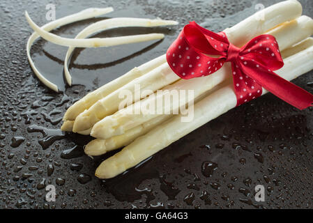 Weißer Spargel mit roten Bogen und schälen auf nasse Teller mit Wassertropfen Stockfoto