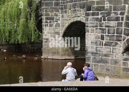 Paar genießt einen Drink am Fluss in Hebden Bridge Stockfoto