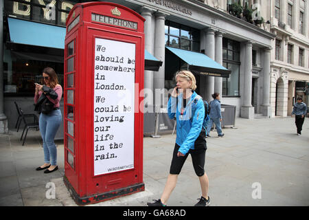 Eine Frau auf einem Handy-Pass mit einem Zitat auf eine rote Telefonzelle am Haymarket in der Londoner Innenstadt. Stockfoto