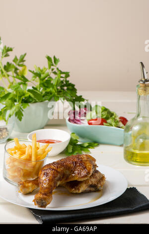 Gebratene Hähnchenschenkel und Pommes Frites und Salat aus Kopfsalat und Tomaten auf weißer Holztisch Stockfoto
