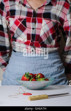 Schale mit frischen Erdbeeren und eine Frau mit Küchenschürze, stehen vor dem Tisch, unkenntlich Stockfoto
