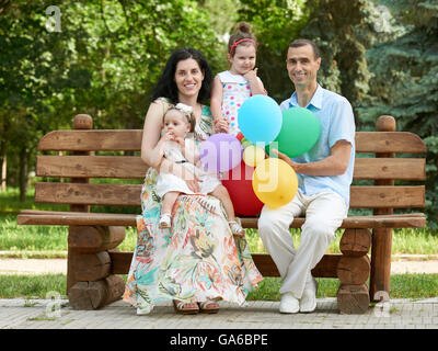 glückliche Familie sitzen auf Holzbank im Stadtpark, Sommersaison, Kind und Elternteil, Gruppe von vier Personen Stockfoto