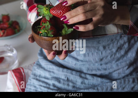 Schale mit Erdbeeren in den Händen einer Frau mit Schürze, am Tisch sitzen Stockfoto