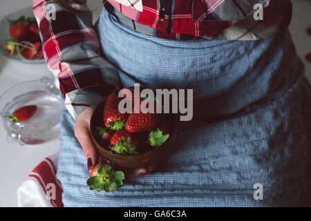 Schale mit Erdbeeren in den Händen einer Frau mit Schürze, am Tisch sitzen Stockfoto