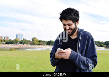 Lässige hispanische junger Mann mit einem Smartphone in einem Park. Stockfoto