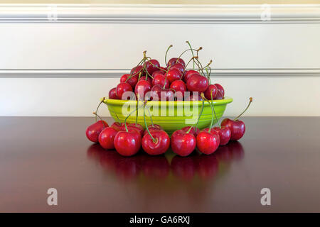 Haufen von Bing Kirschen in grüne Schüssel und auf Holztisch mit Reflexion Stockfoto