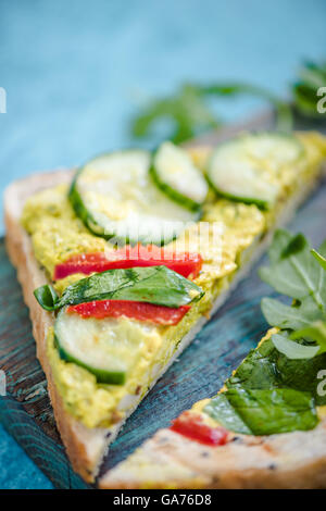 Brot-Dreieck mit Huhn und Rucola auf rustikalem Holzbrett Stockfoto