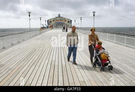 Eine Familie rast heute am Pier in Bournemouth in Dorset gegen den Wind, wo der goldene Sand aufgrund des schlechten Augustwetters fast vollständig verlassen war. Stockfoto