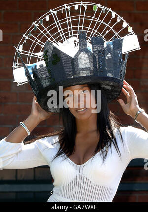 Kopfdrehmütze für Ladies Day bei York Races, da Rochelle Wood einen Hut trägt, der das York Eye Wheel zeigt, mit einem Schirm, der die York City Walls auf der York Racecourse zeigt. Stockfoto