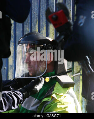 Ein Polizeibeamter legt eine Schutzmaske auf einen Demonstranten, bevor er ein Schloss durchschneidet, das ihn mit den Toren verbindet, nachdem sich eine Gruppe von Klimademonstranten vor dem Biggin Hill Airport in Kent angekettet hatte. Stockfoto