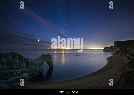 Sterne und Milchstraße über Durdle Door und der Jurassic Coast, mit den Lichtern von Weymouth und Portland, Dorset, England, UK, Dezember 2013. Stockfoto