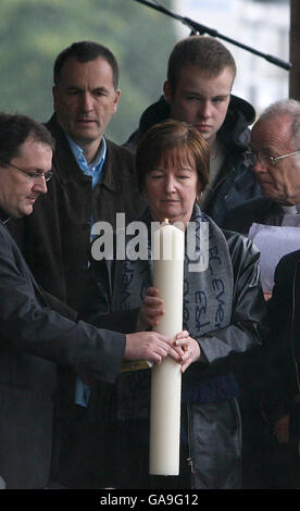 MIT ZUSÄTZLICHEN BILDUNTERSCHRIFTEN ÜBERLIEFERT MELANIE Jones die Mutter des ermordeten Schuljungen Rhys Jones hält eine Kerze mit Pater Andrew Unsworth, während Ehemann Stephen und Sohn Owen auf eine Gemeinschaft Vigil im Croxteth Park, Liverpool, schaut. Stockfoto