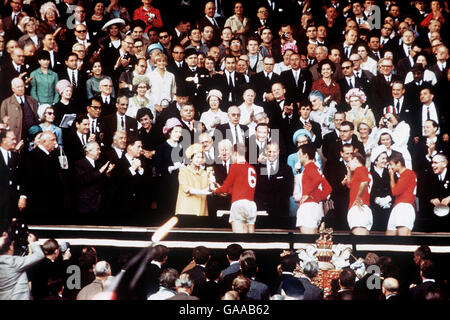 (L-R) Königin Elizabeth II. Überreicht dem englischen Kapitän Bobby Moore die Jules-Rimet-Trophäe, die vom Rest des englischen Teams beobachtet wird Stockfoto