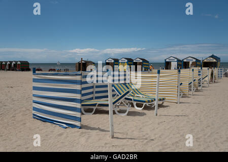 Old fashioned gestreifte Badekabinen, Schirme und Windbreaker säumen den Sandstrand entlang der Küste von De Panne, Belgien. Stockfoto