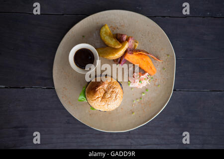 Ein gesunder, hochwertiger, magerer Burger in selbstgebackenem Brot serviert mit Süßkartoffelfries und Kartoffelkeilen, keine Menschen, Nahaufnahme, neutraler Hintergrund Stockfoto