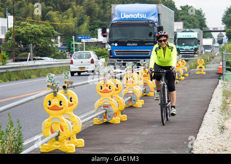 Ein Weibchen touring Radsportler, die auf einem Radweg von Verkehr durch eine gelbe Ente Barriere getrennt. Stockfoto