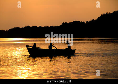 Holz Ruderboot auf See in den späten Abend mit zwei Mädchen und Vater-Menschen-Silhouetten Stockfoto