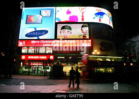 Ein paar halten an, um die erste persönliche Nachricht zu bewundern, die auf dem neuen Piccadilly Lights-Schild im Piccadilly Circus im Zentrum von London veröffentlicht wurde. Stockfoto