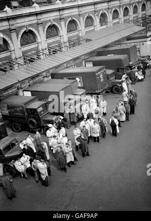 Smithfields weiß beschichtete Fleischporteure stehen bei leeren Fleischwagen in Smithfield. Stockfoto