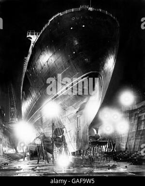 Über dem King George V Trockendock in Southampton thront der gigantische Rumpf des Cunard-White Star Liners Queen Mary, der vom Nachthimmel von Flutlichtern umragt wird, während sie eine sechswöchige Überholung und Renovierung durchläuft. Stockfoto