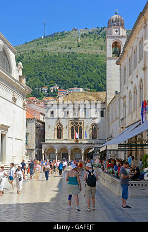 Straßenszene von Touristen in der Altstadt von Dubrovnik in Kroatien mit der Sponza-Palast und der Glockenturm in Luza Square blauer Himmel sonniger Tag Stockfoto