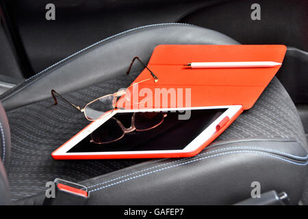 Apple iPad Pro Tablette 9,7 Zoll in rotem Einband verließ am Kindersitz mit dedizierte weißen Apple Bleistift wertvolle Eigenschaft & Sachen links auf dem Display im Auto Stockfoto