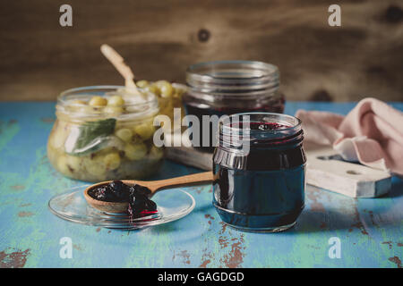 Verschiedenen Beeren-Gelee. Hausgemachte Bio Heidelbeere, Himbeere und Stachelbeere Marmelade in Gläsern auf blauen rustikalen Holztisch Stockfoto