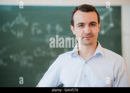 Porträt des jungen glücklich lächelnden Lehrer oder Schüler Mann stand in der Nähe Tafel Hintergrund Stockfoto