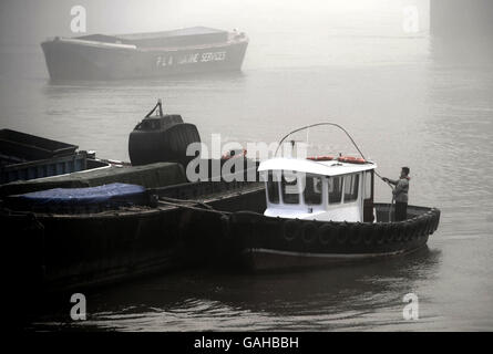 Ein Flussschiffer arbeitet auf der Themse, in der Nähe des Südufers im frühen Morgennebel. Stockfoto