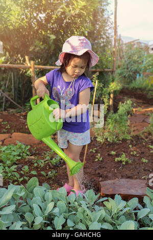 Kleines Mädchen mit Gießkanne Wasserpflanzen im Garten, Montessori-Bildungskonzept Stockfoto