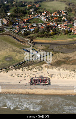 Strandhütten in Walberswick an der Küste von Suffolk, in denen die Dorfbewohner heute einen Menschen bildeten, "Save Our Shoreline" (SOS), um gegen die Entscheidung des Ministeriums für Umwelt, Ernährung und ländliche Angelegenheiten (DEFRA) zu protestieren, die Finanzierung für die Aufrechterhaltung der Meeresverteidigung, eines Schindelkamms und Flutbänke entlang seiner Mündung zurückzuziehen. Es wird befürchtet, dass dieses Gebiet von außergewöhnlicher natürlicher Schönheit schließlich untergetaucht wird. Stockfoto