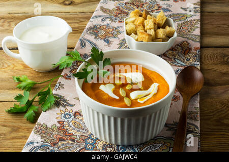 Herbstliche würzige Kürbis squash Cremesuppe mit Sahne, Petersilie und Kürbiskernen und in der weißen Schale, Creme in einem Milchkännchen und cro Stockfoto