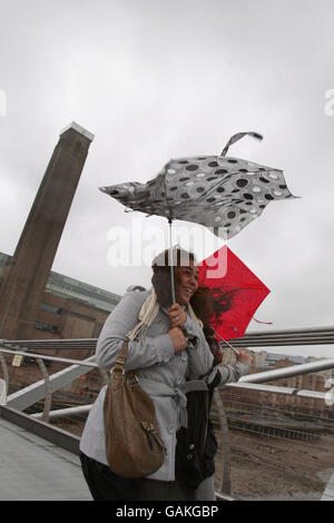 Zwei Frauen kämpfen heute bei einem Regenschauer, um sich an ihren Schirmen festzuhalten, als sie über die Millennium Bridge im Zentrum Londons gehen. Stockfoto