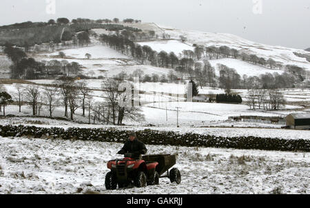 Bauer Peter Laidlaw von der Craigannet Farm füttert Hochlandrinder auf den Hügeln, die den Carron Dam-Stausee in der Carron Valley Fishery, Schottland, überblicken, nachdem heute Schnee gefallen ist. Stockfoto