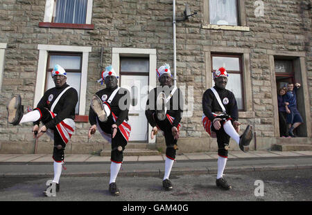 Mitglieder der Britannia Coconut Dancers of Bacup auf den Straßen in der Nähe von Bacup während ihres traditionellen jährlichen Ostersamstags-Tanzes. Es wird angenommen, dass die geschwärzten Gesichter einen heidnischen oder mittelalterlichen Hintergrund widerspiegeln könnten, als es getan wurde, um die Tänzer vor bösen Geistern zu verbergen. Alternativ kann es einen Bergbau-Hintergrund widerspiegeln. Stockfoto