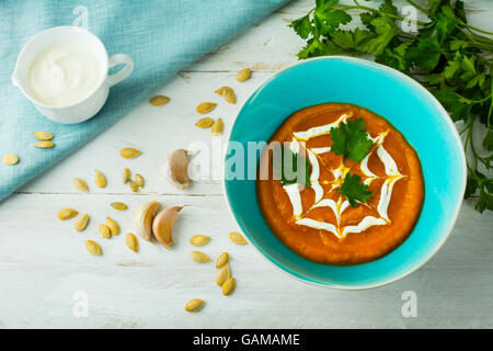 Cremige Kürbis Squash Gemüsesuppe garniert mit Sahne in einem türkisfarbenen Teller, Kürbiskerne, Knoblauch und Petersilie, Ansicht von oben Stockfoto