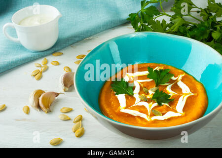 Kürbis squash cremige Gemüsesuppe, garniert mit Sahne in einem Türkis Teller, Kürbiskerne, Knoblauch und Petersilie auf weißem Holz b Stockfoto