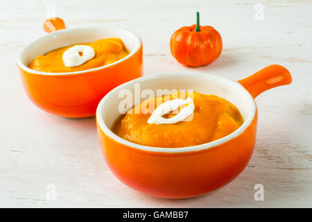 Zwei Portionen Gemüse Kürbis-Kürbis-Suppe mit Sahne in einem Teller mit Griff, Orange hautnah Stockfoto