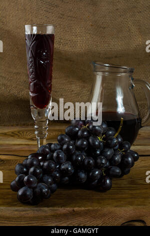 Dunkle Traube und einem Glas Wein auf einem dunklen Hintergrund aus Holz. Haufen von Trauben. Cluster-Trauben.  Bündel Weintrauben. Trauben. Gr Stockfoto