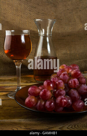 Rote Weintrauben und einem Glas Wein auf einem dunklen Hintergrund aus Holz. Cluster von Trauben. Haufen von Trauben. Cluster-Trauben.  Haufen Stockfoto