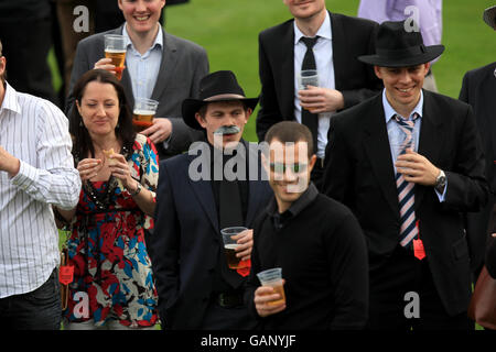 Racegoers genießen einen Drink, während die Saw Doctors während eines Konzerts am Ende des Gold Cup Meetings im Sandown Park auftreten. Stockfoto